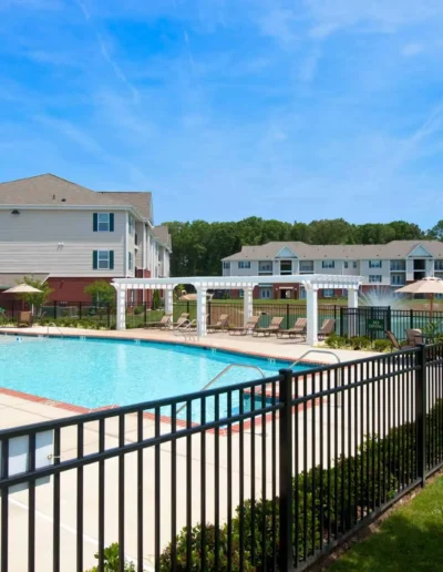 An outdoor recreation area featuring a fenced-in swimming pool, a white pergola-shaded lounge area